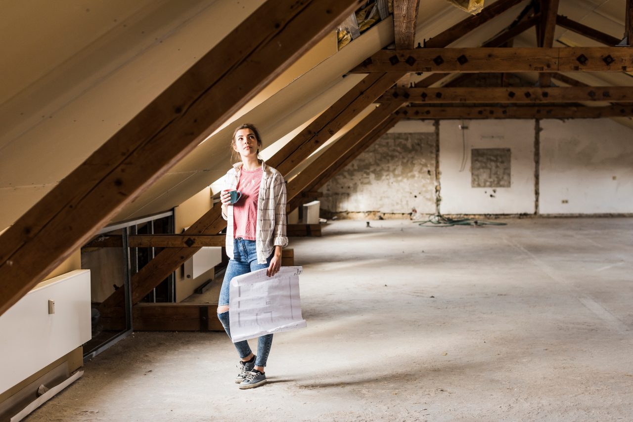 Frau auf dem Dachboden mit einem Kaffee und einem Bauplan in der Hand